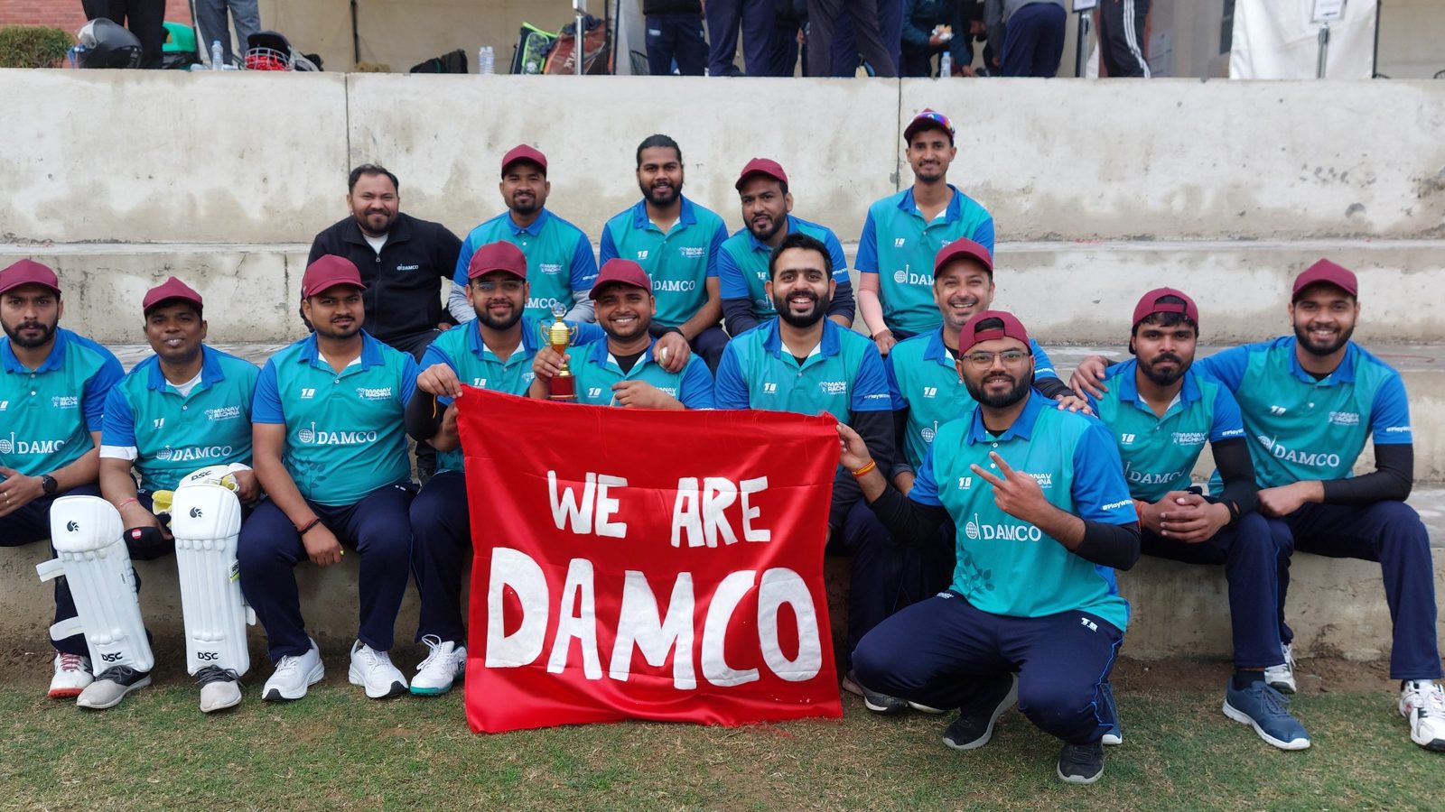 Team Damco's cricket squad holding a We are Damco banner